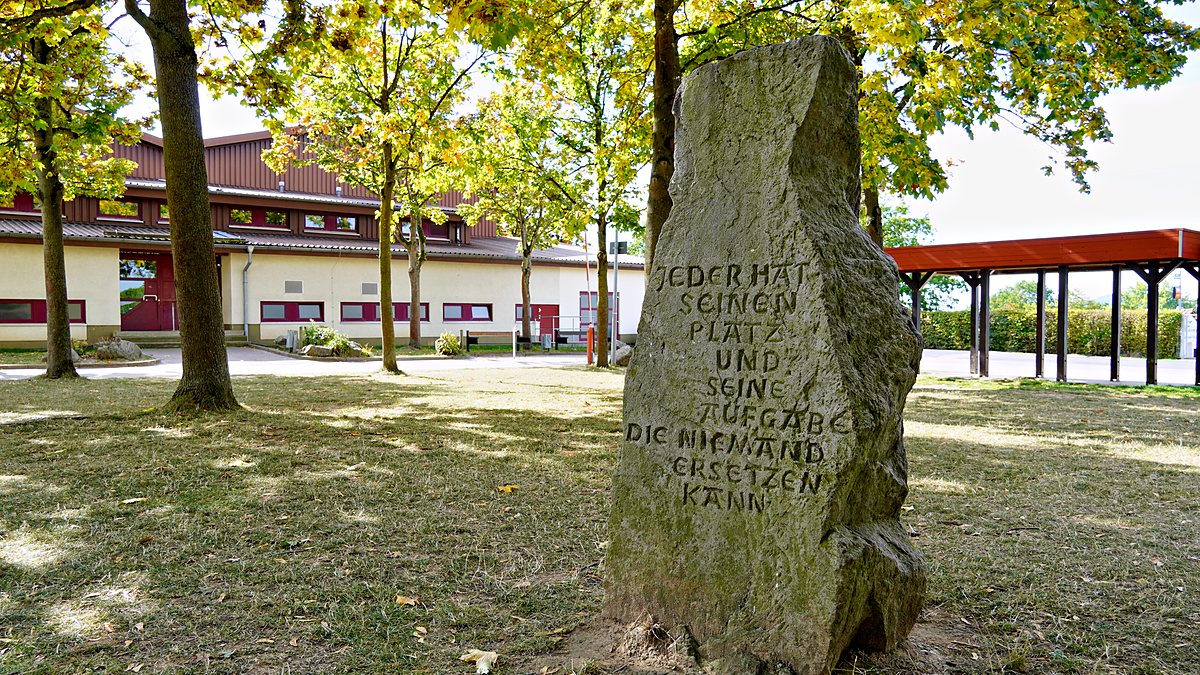 Stein auf dem Schulhof mit der Inschrift „Jeder hat seinen Platz und seine Aufgabe, die niemand ersetzen kann“