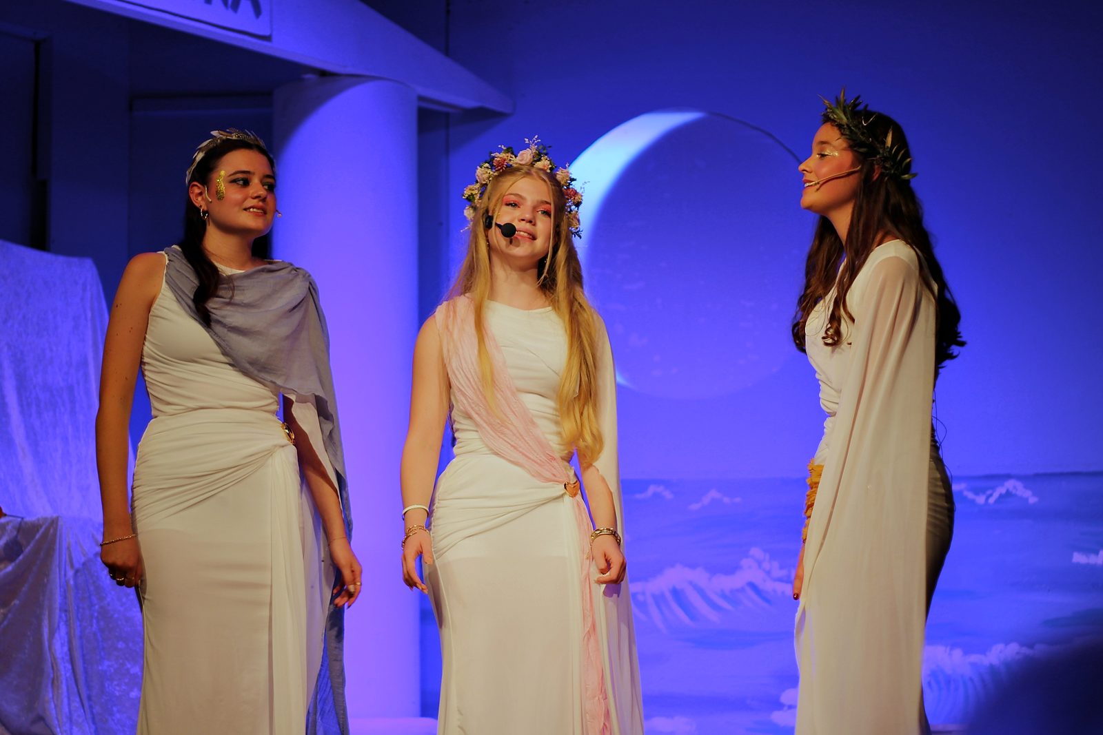 Drei Göttinnen in hellen Gewändern mit Blumenkränzen vor dem Tempel der Athena