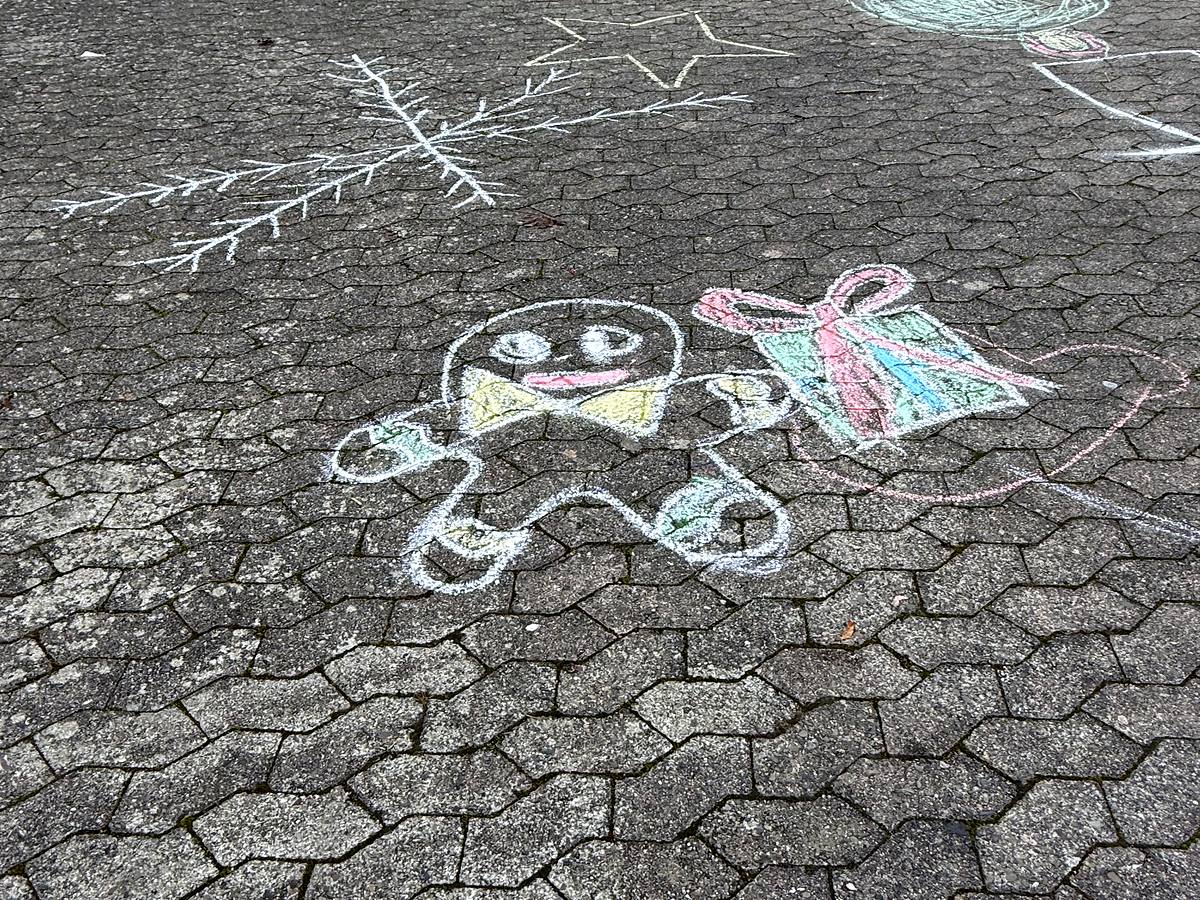 Mit Kreide auf den Schulhof gemalt: ein Lebkuchenmann neben einem Geschenk, daneben ein Schneekristall